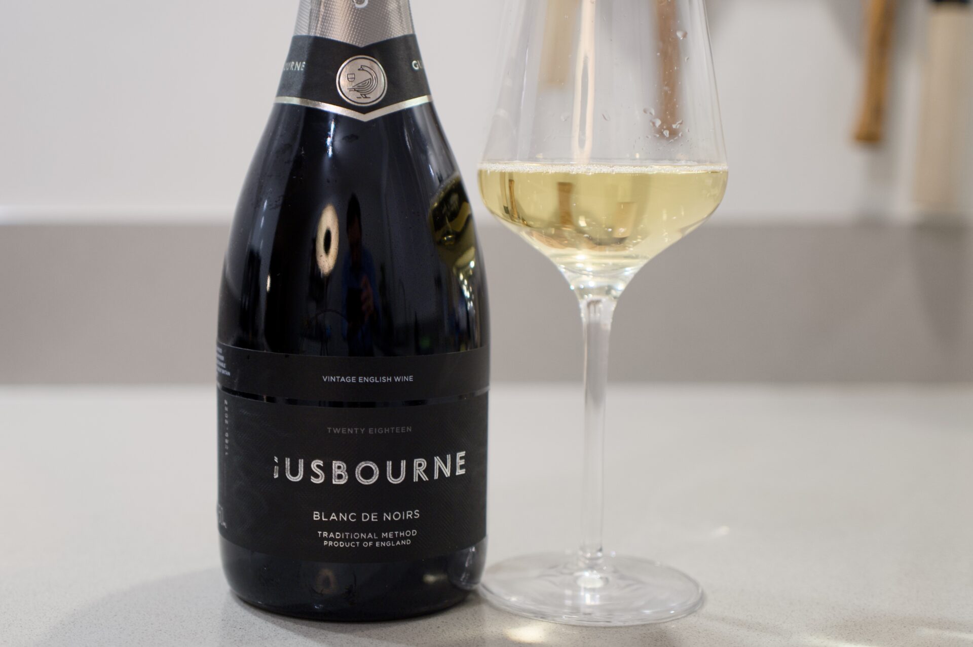 Gusbourne Blanc de Noirs 2018 fles en glas met Engelse wijngaard