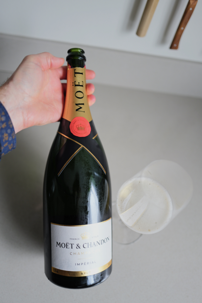 Hand die de magnum Moët & Chandon Brut Impérial vasthoudt naast twee glazen op een aanrecht